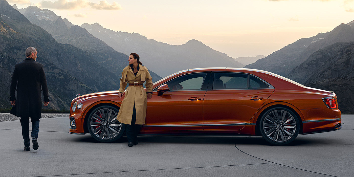Bentley Gold Coast (Australia) Bentley Flying Spur Speed parked in Orange Flame coloured exterior parked, with mountainous background and two people in view.