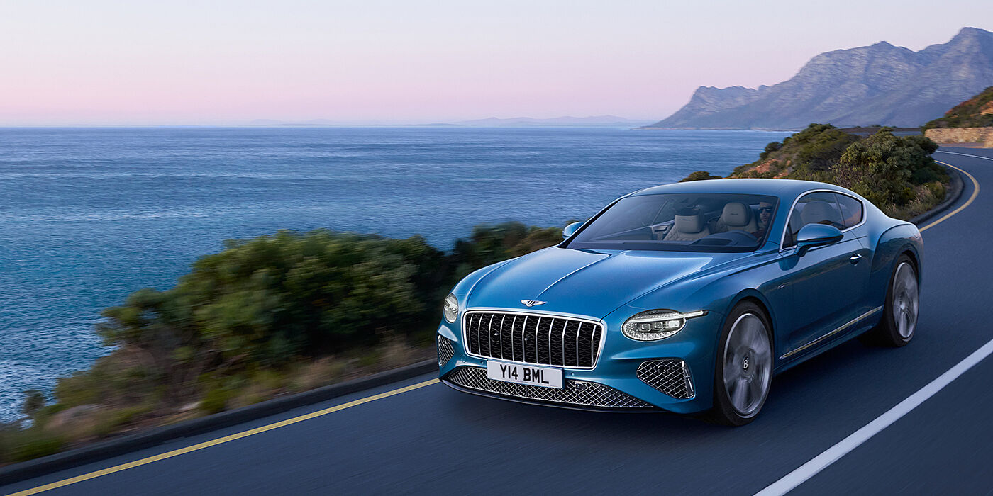 Bentley Gold Coast (Australia) New Bentley Continental GT Azure coupe in Light Windsor blue paint with 22 inch Azure wheels and chrome grill, driving dynamically by the sea