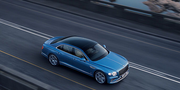 Bentley Gold Coast (Australia) New Bentley Flying Spur Azure sedan in Light windsor blue paint by Mulliner, with 22 inch Azure wheels seen from overhead driving dynamically on a country road