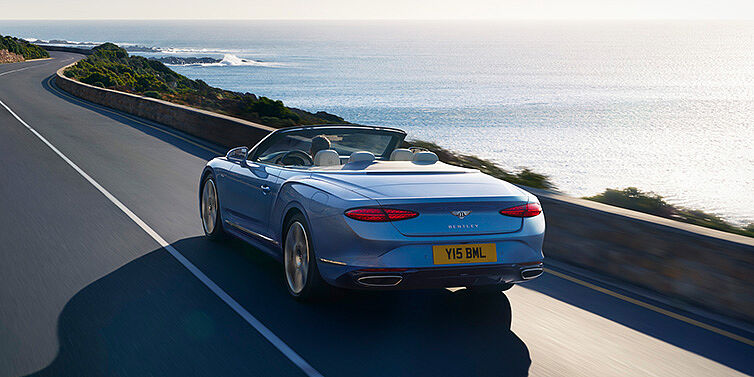 Bentley Gold Coast (Australia) New Bentley Continental GTC Azure convertible rear view in Light Windsor blue paint with 22 inch ten spoke wheels driving dynamically on an ocean road in the sunshine