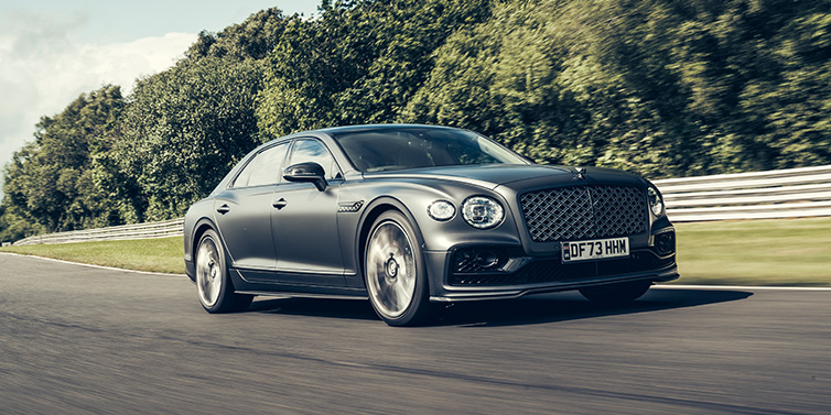 Bentley Gold Coast (Australia) Bentley Flying Spur Mulliner sedan front three quarter in dark grey paint driving dynamically by some trees on a track