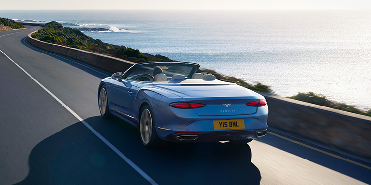 Bentley Gold Coast (Australia) New Bentley Continental GTC Azure convertible rear view in Light Windsor blue paint with 22 inch ten spoke wheels driving dynamically on an ocean road in the sunshine