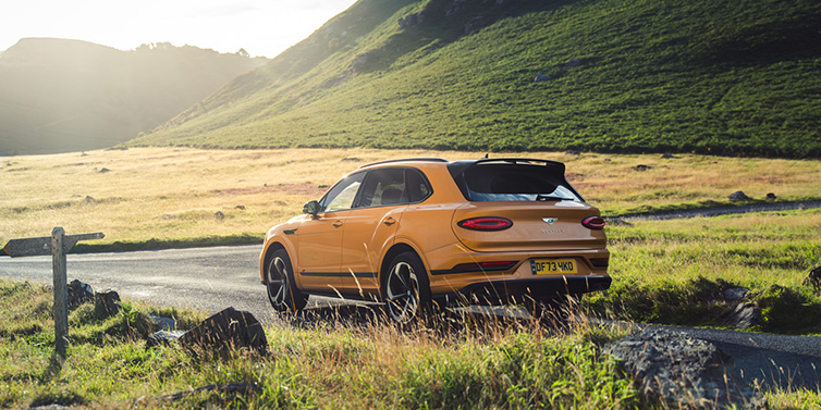 Bentley Gold Coast (Australia) Bentley Bentayga S SUV rear three quarter in Sunburst Gold paint on a road surrounded by green hills