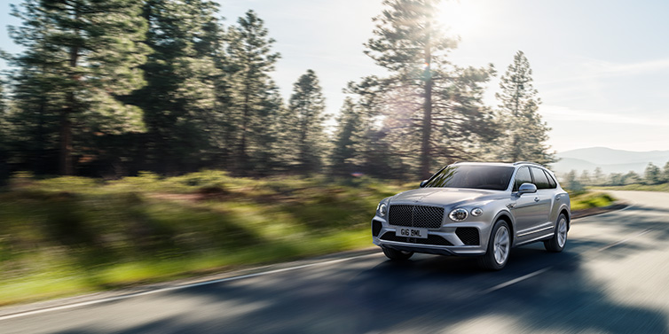 Bentley Gold Coast (Australia) Bentley Bentayga SUV front three quarter in Moonbeam silver paint driving dynamically along a tree-lined road