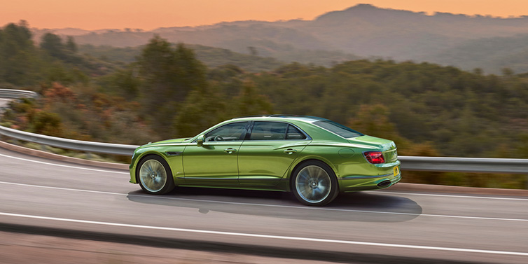 Bentley Gold Coast (Australia) Bentley Flying Spur Speed sedan side profile in Tourmaline Green paint driving dynamically on a mountain road at sunset